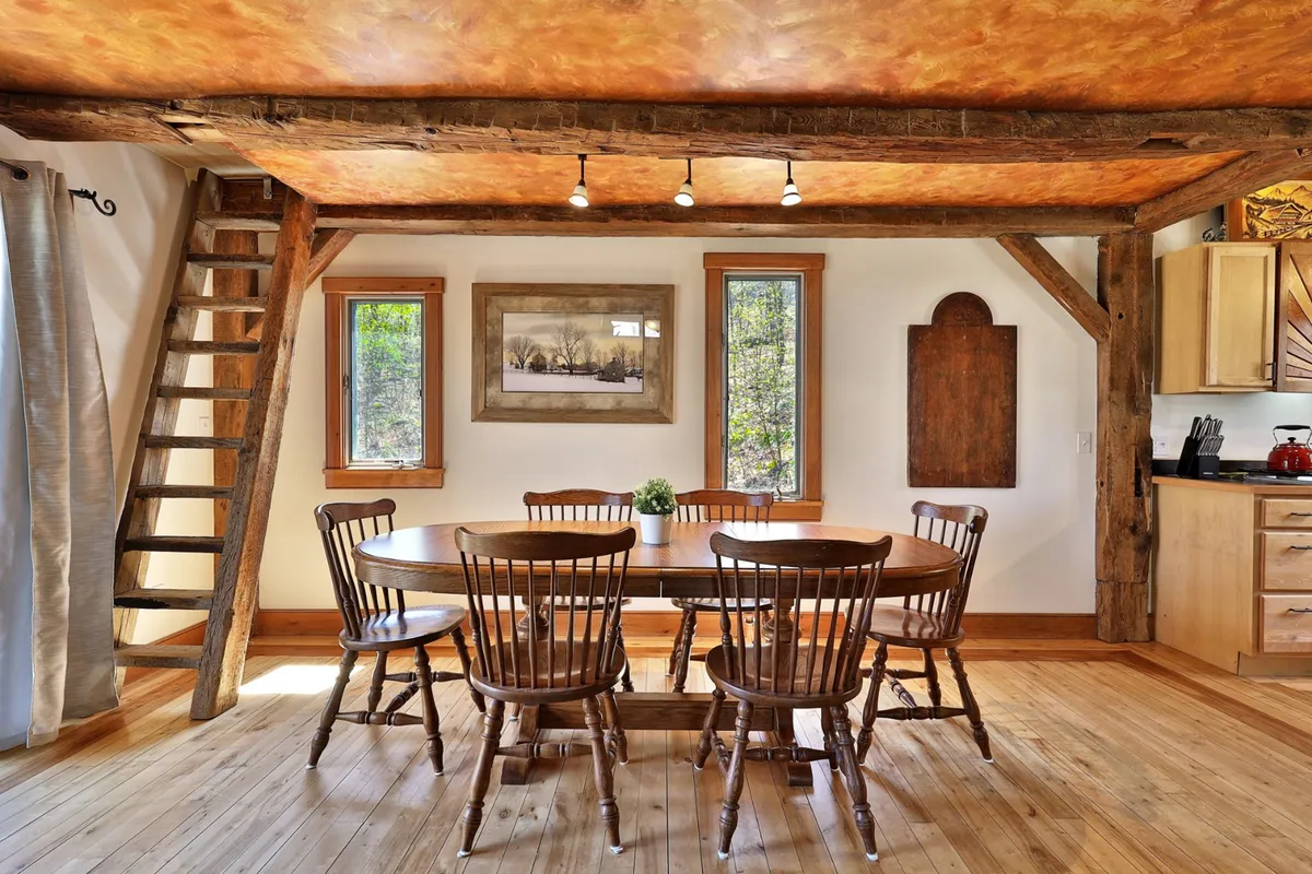 A bright and welcoming dining space featuring a large wooden table, a sturdy ladder (hinting at bunk or loft areas), windows letting in natural light, and local artwork. The setup is ideal for group meals, family celebrations, or morning gatherings.