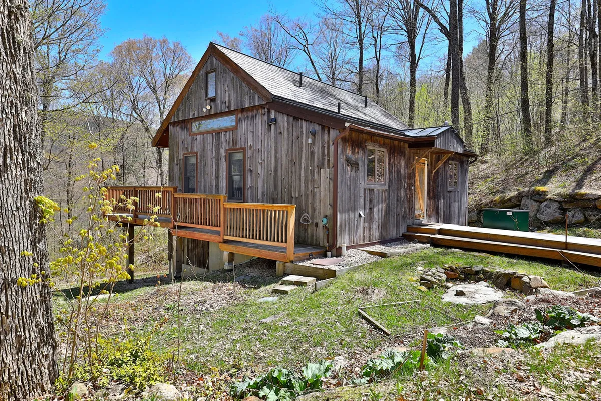 This image showcases the wooden exterior of the house, a deck with railing, and landscaped yard surrounded by trees. The deck suggests a spot for morning coffee or evening gatherings, connecting indoor comfort with outdoor adventure.
