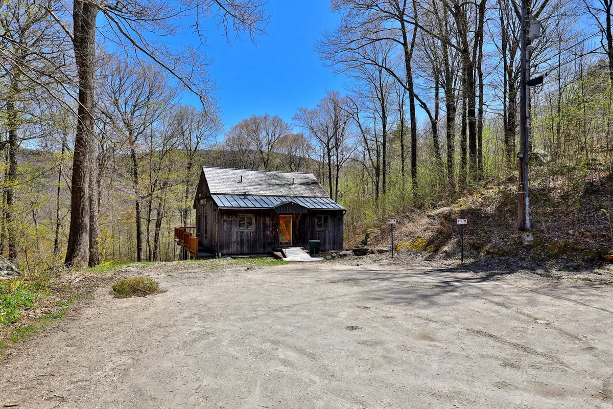 The rustic cabin is framed by surrounding trees and a dirt path, reinforcing the sense of seclusion and immersion in nature. The peaceful mood invites thoughts of relaxing after a day on the slopes or enjoying a quiet morning before heading out.