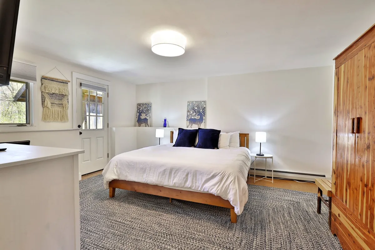 A light-filled bedroom with a double bed, nightstands, tasteful artwork, and a wardrobe. The space is bathed in sunlight, suggesting a safe and peaceful retreat for guests.