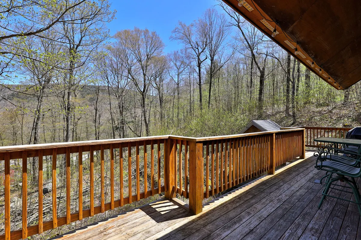 A wooden deck with a classic railing, positioned to overlook a lush, natural landscape. Outdoor furniture invites guests to relax, enjoy the view, or share a quiet moment amid the trees.