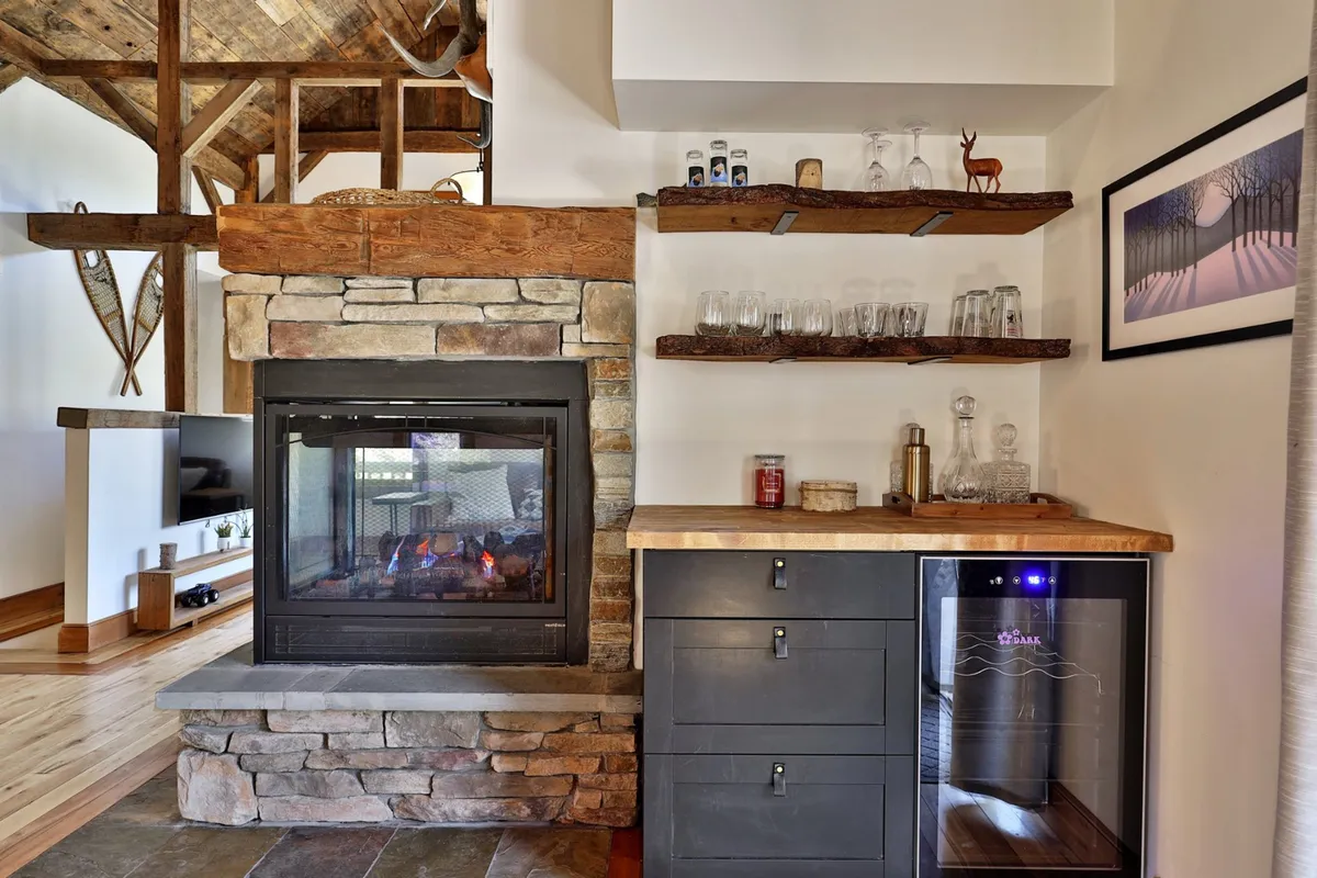 An inviting interior space with a glowing fireplace, shelves stocked with glasses, and a wine cooler nearby. The setup evokes the idea of enjoying drinks in a cozy ambiance, perfect for socializing before a night out.