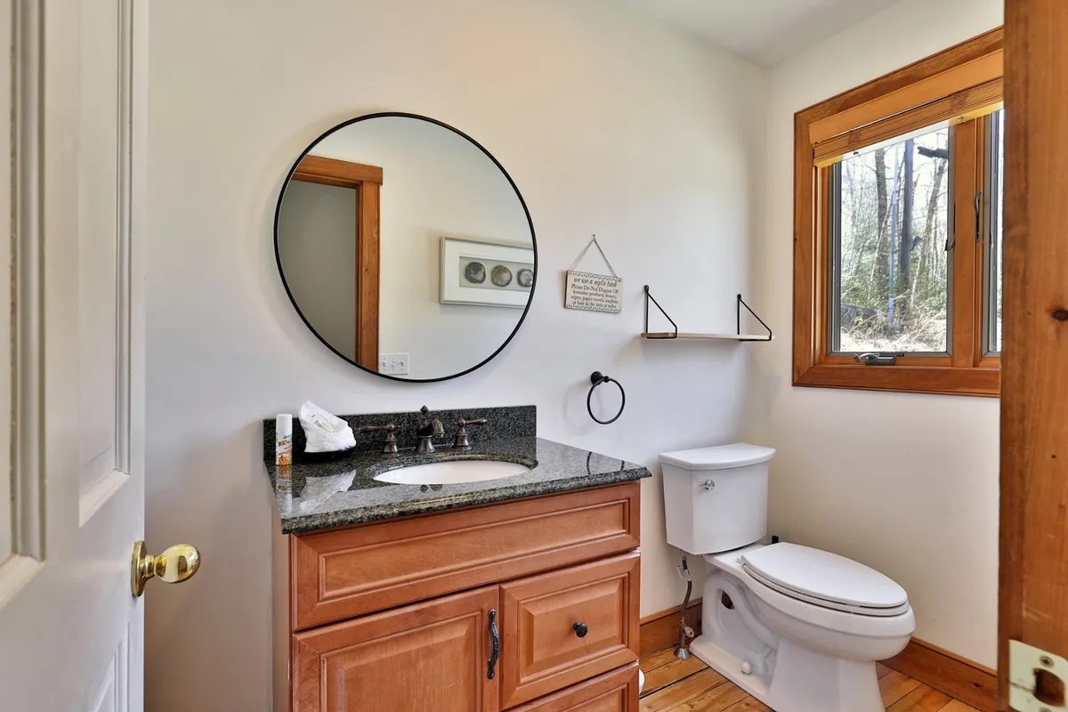 A well-lit laundry area with granite countertops, wooden cabinetry, a round mirror, and a window for natural light. This practical space supports easy in-unit laundry for families and groups.