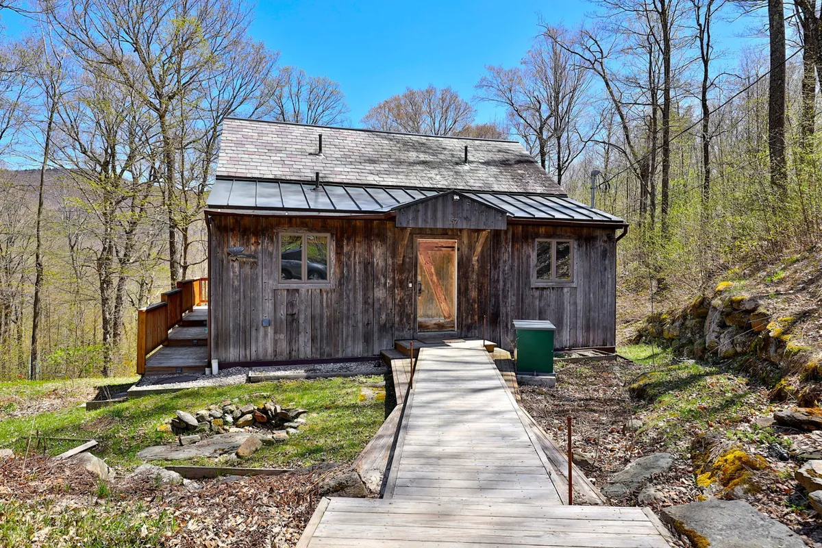 This image features the exterior of The Wobbly Cabin, showcasing its charming wooden structure set among tall trees and a welcoming walking path. The view emphasizes accessibility to nature and the tranquil surroundings, highlighting the cabin as a cozy retreat near outdoor adventure.