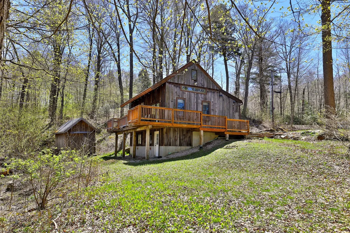 A view of the cabin’s wooden deck set amid abundant greenery and trees, with space for lounging or group activities. The seamless integration of the deck with the natural environment creates a perfect spot for stargazing or enjoying seasonal changes.