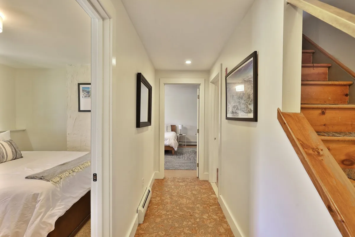 This image shows a wooden staircase, framed artwork, and bedroom doors leading off a small hallway. The area is functional and transitional, capturing the movement from one part of the home to another.