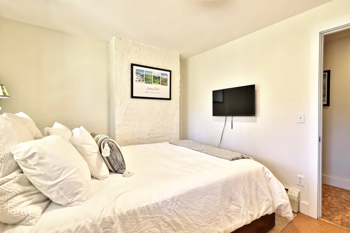 A cozy bedroom featuring a comfortable bed with plush pillows, soft lighting, and relaxing décor. The presence of a wall-mounted television and subtle artwork adds to the inviting, secure atmosphere.
