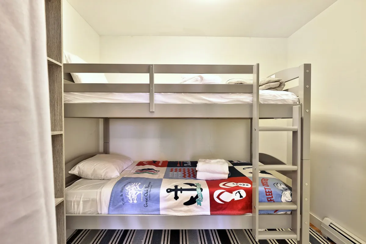 A cozy bedroom featuring a bunk bed with colorful bedding and built-in shelves, designed to accommodate children or friends. The playful decor and practical sleeping arrangement make it ideal for families or groups, emphasizing privacy and comfort.