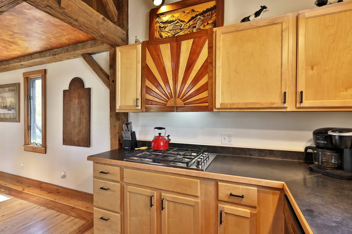 This image presents the fully equipped kitchen with striking wooden cabinets featuring a sunburst design, a red kettle on the stove, and a coffee maker on the counter. The kitchen feels cozy and inviting, with plenty of natural light and ample space for cooking and entertaining.